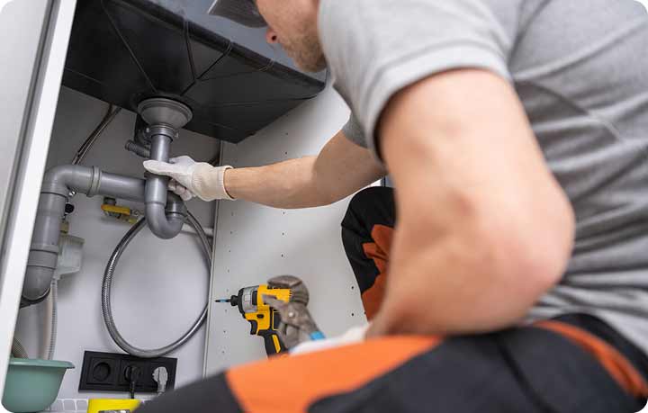 Tip Top Plumbing & Restoration specializes in precise leak detection services in Broward County, FL. The image clearly shows a professional plumber inspecting plumbing pipes under a kitchen sink, utilizing specialized tools. Tip Top Plumbing, conveniently located at 3361 N Dixie Hwy, Oakland Park, offers efficient leak detection and can be reached at 954-471-4036.