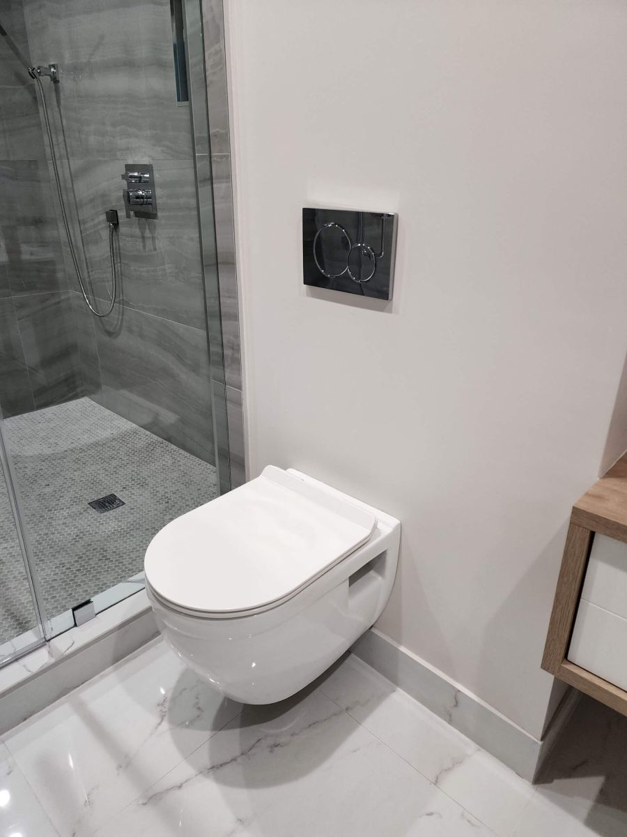 Modern bathroom with wall-mounted toilet, dual-flush actuator, and glass shower—ideal for toilet installation, leak repairs, and bathroom plumbing services by Tip Top Plumbing & Restoration in Broward County, FL.