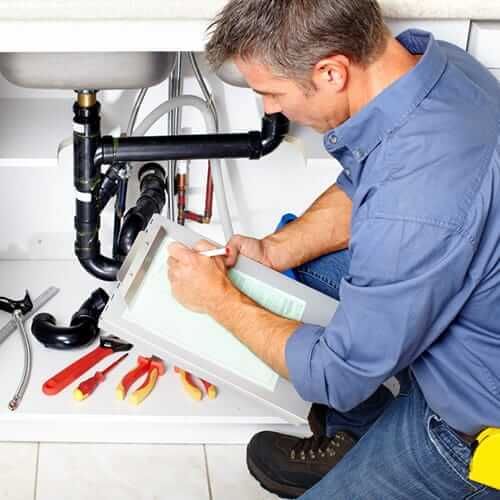 Professional plumber inspecting kitchen drain system under a sink in Hillsboro Beach, FL, representing local plumbing and restoration services.