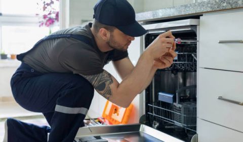 Tip Top Plumbing & Restoration technician installing a dishwasher in a modern kitchen in Miramar, FL, with focus on connecting water and drainage lines.